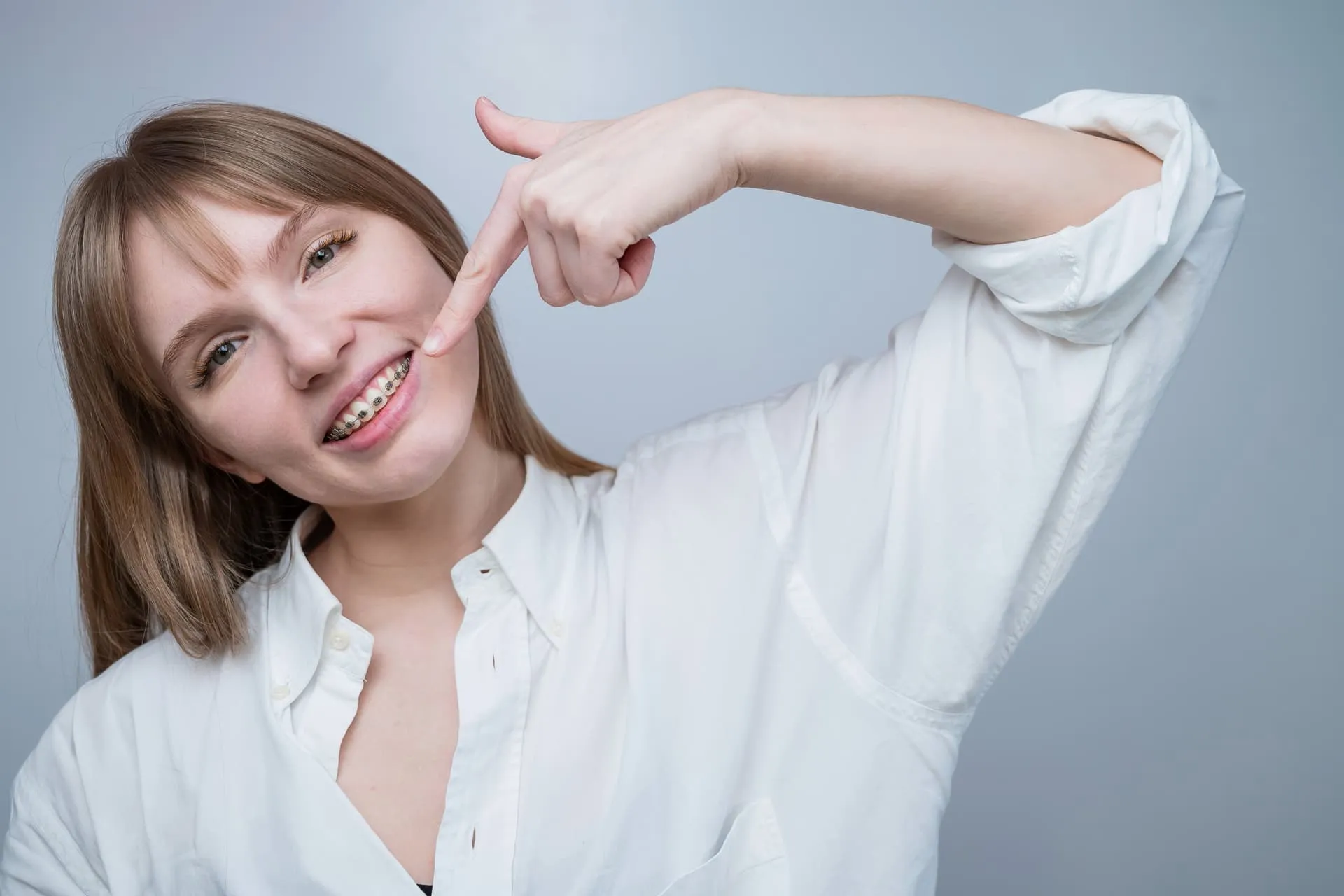 Joven sonriendo y señalando sus brackets de ortodoncia